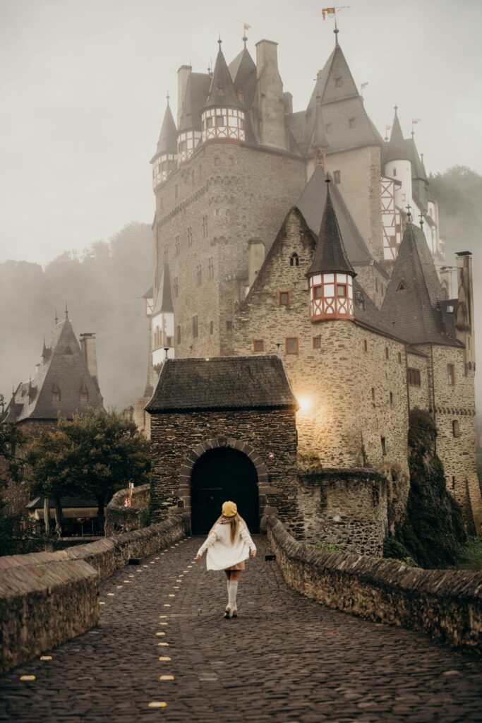 pexels photo 6023542 6023542 A woman walking towards the historic Eltz Castle on a foggy morning in Germany.